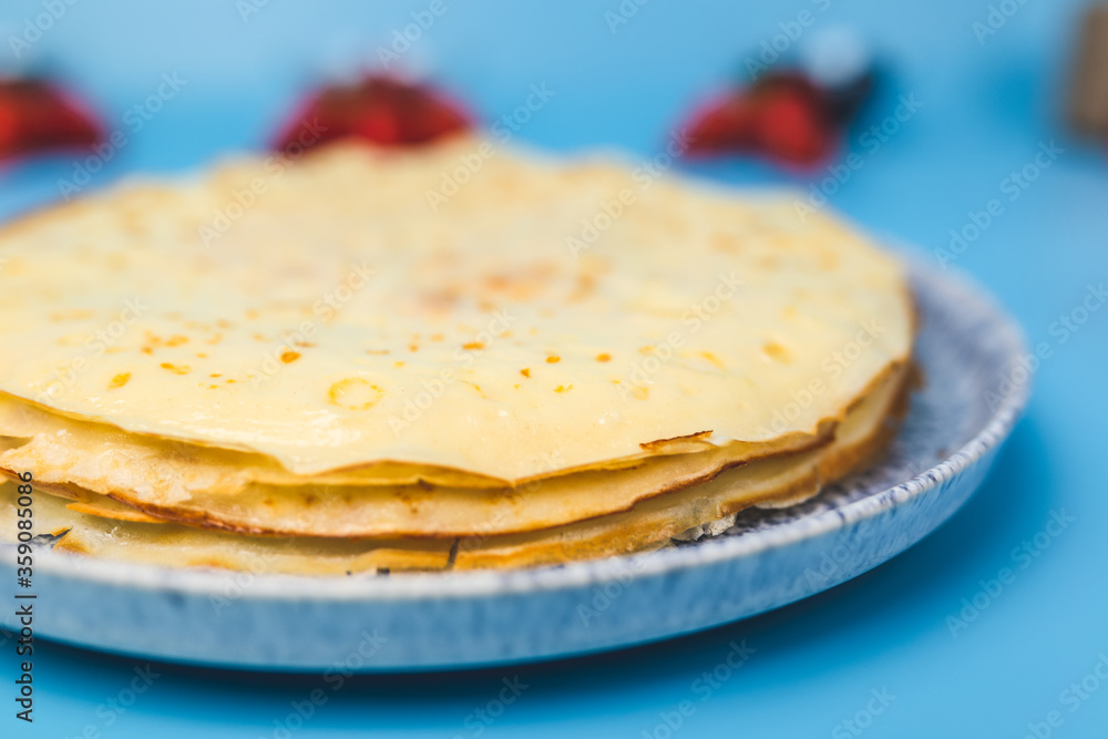 Close-up of a pack of French Crepes in a serving plate with berries on the side on a blue background. Crepe with strawberries, blueberries, rose berries, sliced bananas. Close-up of a pack of French Crepes in a serving plate with berries on the side on a blue background. Crepe with strawberries, blueberries, rose berries, sliced bananas.