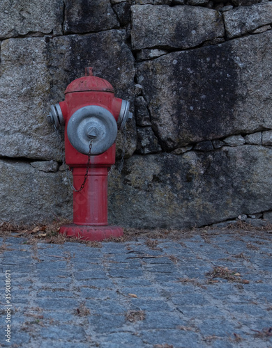 Vintage, red metal fire hydrant against an old stone wall in rural Portugal. Close up.