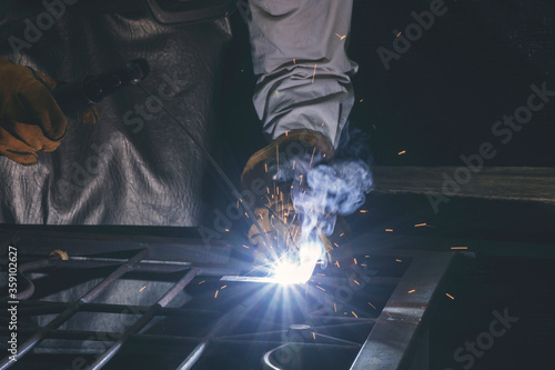 Hand of man wear glove working with arc welding machine to weld steel at outdoor. The welder welds steel reinforcement with welding and bright sparks.