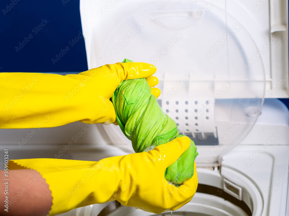 hands of a girl with yellow gloves squeezing a green shirt with foam from a semi automatic washing machine hands of a girl with yellow gloves squeezing a green shirt with foam from a semi automatic washing machine