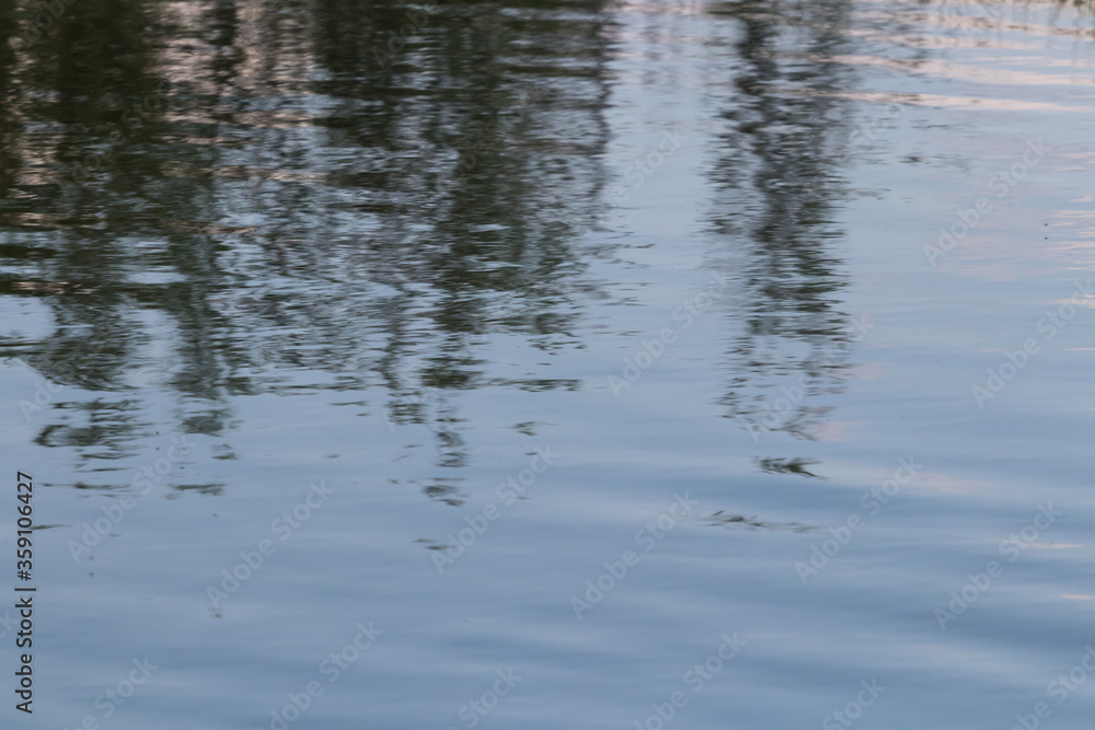 Blurred reflection of dark trees on the water surface Blurred reflection of dark trees on the water surface