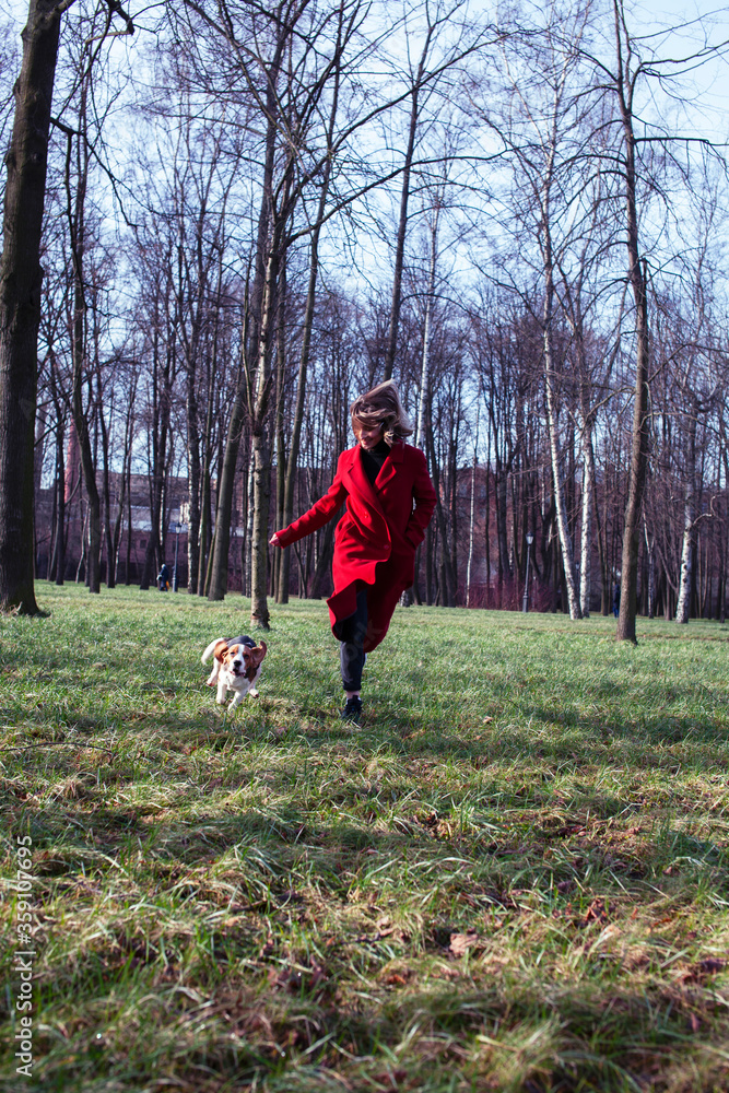 pretty young girl in redd coat playing with dog outside in green park, lifestyle people concept