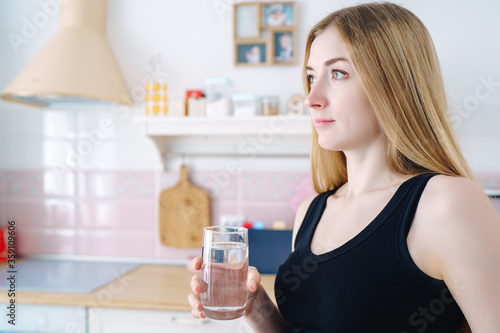 young beautiful woman drinks a glass of water in the kitchen , close-up, concept of a healthy lifestyle, water balance
