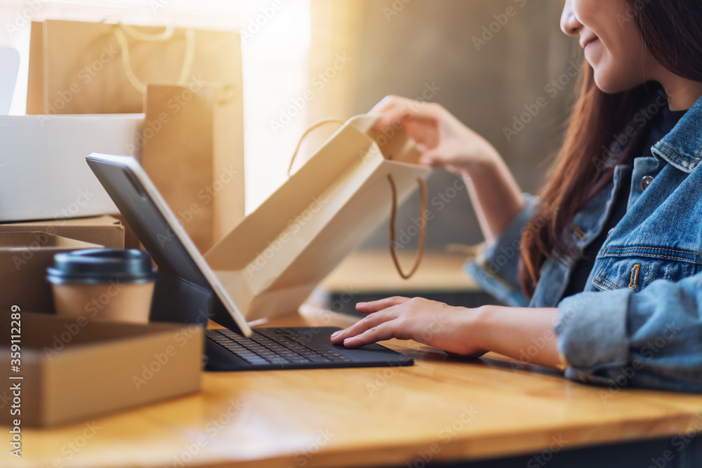 Closeup image of a young woman using tablet pc for online shopping , opening shopping bags and postal parcel box on the table Closeup image of a young woman using tablet pc for online shopping , opening shopping bags and postal parcel box on the table