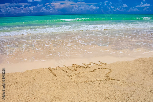 Tropical beach in Miami with bright blue sky, turquoise water and Miami written on the sand