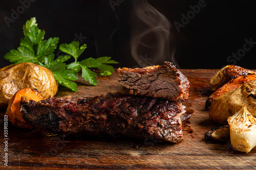 carne asado argentino con papa zanahoria y cebolla sobre madera con fondo oscuro