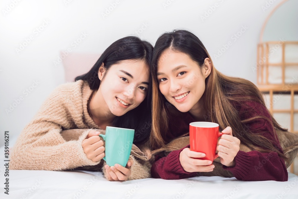 Young beautiful Asian women lesbian couple lover holding coffee cup in bed room at home with smiling face.Concept of LGBT sexuality with happy lifestyle together. Young beautiful Asian women lesbian couple lover holding coffee cup in bed room at home with smiling face.Concept of LGBT sexuality with happy lifestyle together.