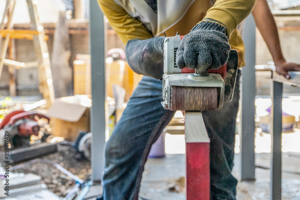 Carpenter is shaving red wood door by his shaving machine in outdoor field with steel pole building structure environment. Carpenter is shaving red wood door by his shaving machine in outdoor field with steel pole building structure environment.