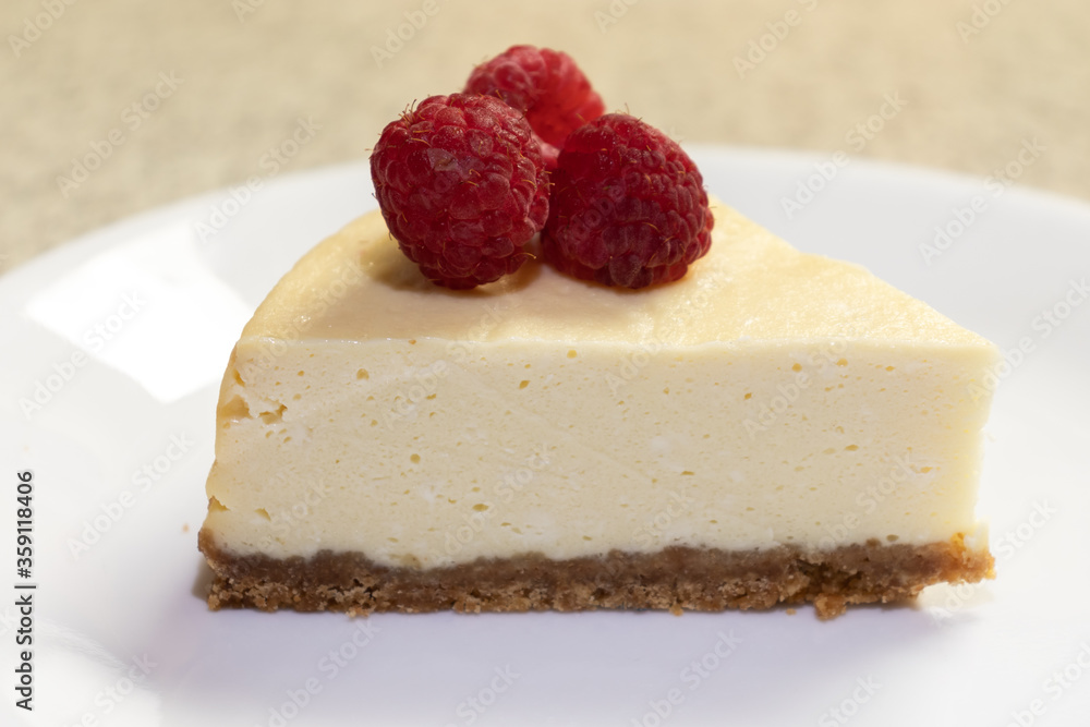 A creamy cheesecake topped with fresh raspberries on a white plate waiting to be served. A creamy cheesecake topped with fresh raspberries on a white plate waiting to be served.