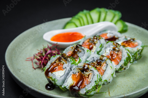 Perfect sushi, traditional Japanese cuisine. Delicious uramaki with sweet and sour sauce on the decorated plate, black background.