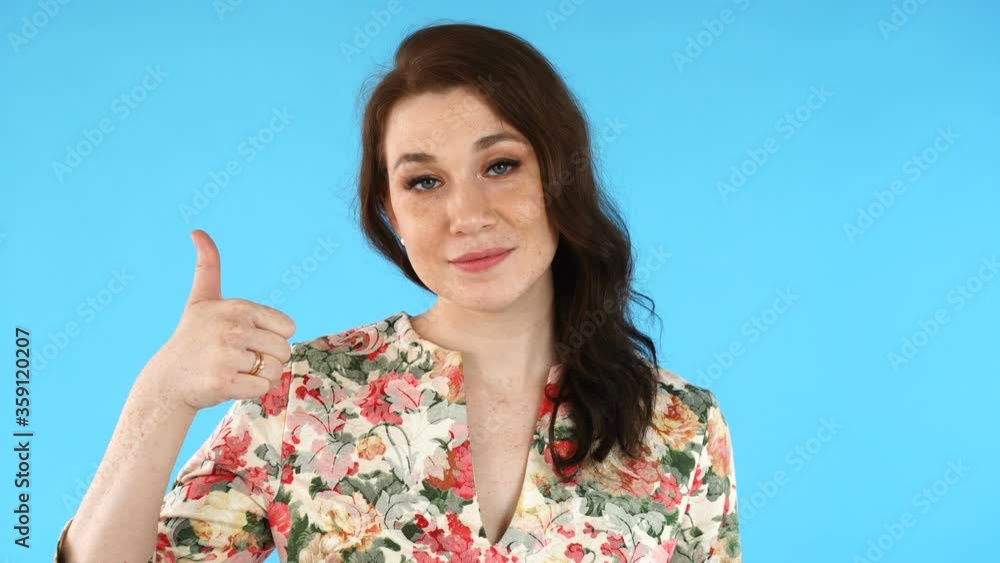 Positive young european woman smiles to camera. Pretty girl showing thumb up sign over blue background. Positive young european woman smiles to camera. Pretty girl showing thumb up sign over blue background.