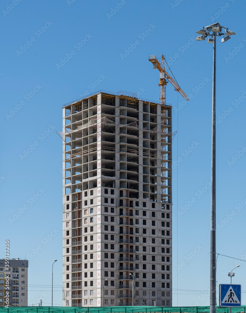 Construction site with a multi-storey residential building under construction and a tower crane against a blue summer sky. Sterlitamak, Republic of Bashkortostan.