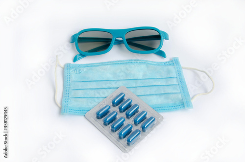 Blue capsule pills, blue protective mask, and blue goggles on a white background. 