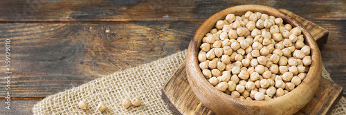 Obraz na płótnie Chickpeas in a wooden bowl on the brown kitchen table. Raw chickpeas close-up. Banner with space for text w salonie