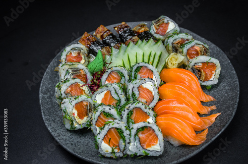 Sushi, traditional Japanese cuisine. Several delicious sushi on the decorated plate, black background. Group of sushi, Urakami, Nigori, Sushi jow, sashimi, tekamaki, etc ...