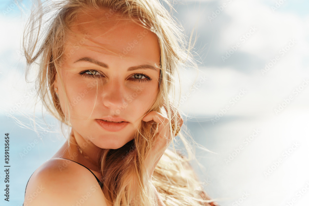 Portrait of a beautiful young blonde with blue eyes against the bright sky and sea horizon. On a bright sunny day. The concept of rest, beauty, travel. Portrait of a beautiful young blonde with blue eyes against the bright sky and sea horizon. On a bright sunny day. The concept of rest, beauty, travel.
