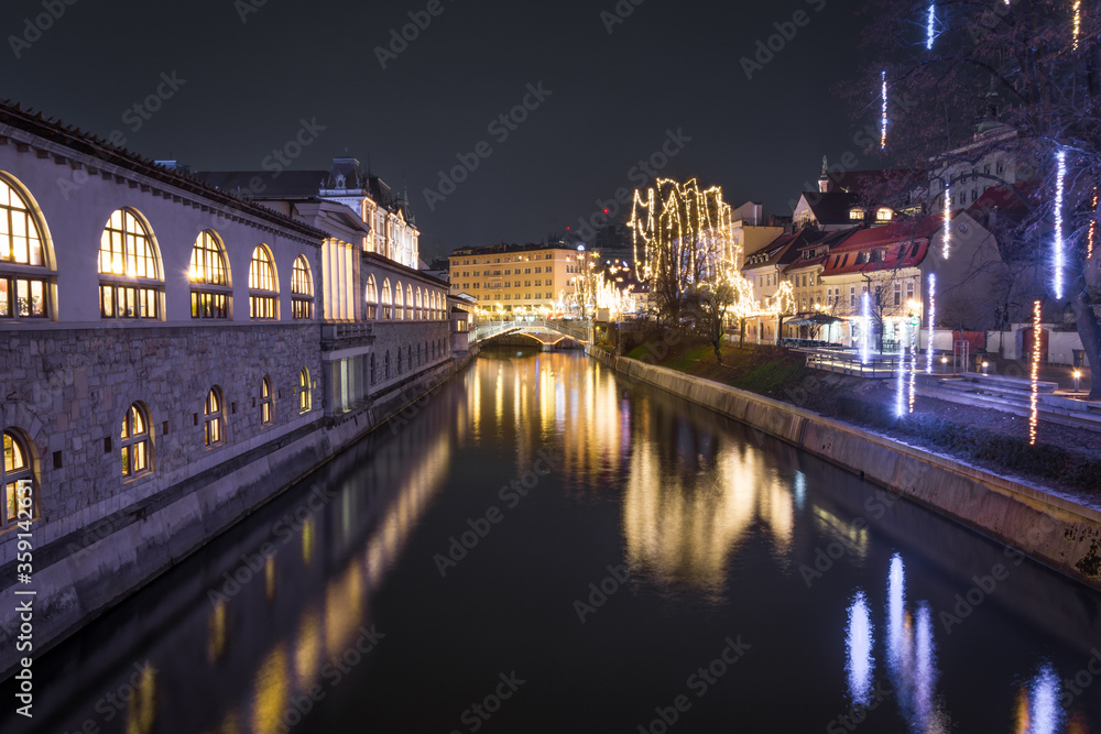 Night view of Ljubljanica River with famous Triple Bridge and medieval colorful buildings in Ljubljana, Slovenia. Reflection in water of Christmas lights in December. Long exposure, wide shot