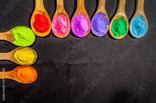 a row of colorful powder colors on wooden spoon in black background . with copy space