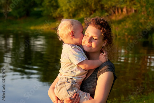 Mom hugs her son on the riverbank at sunset. © Pavlo