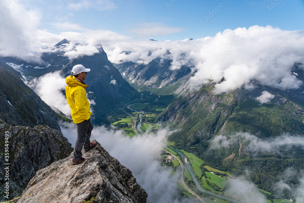 Young Asian man traveller standing on rock looking to mountains, Romsdalseggen hiking trail, Norway, Scandinavia