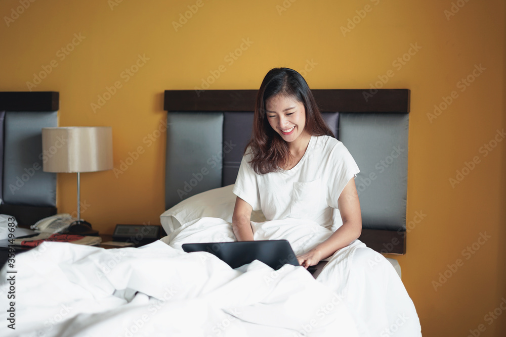 Young happy smiling Asian woman using laptop computer working at home. A woman sitting on bed. Work from home concept Young happy smiling Asian woman using laptop computer working at home. A woman sitting on bed. Work from home concept
