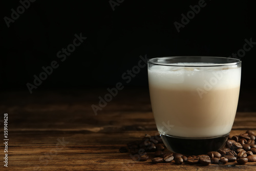 Delicious latte macchiato and coffee beans on wooden table against black background, space for text