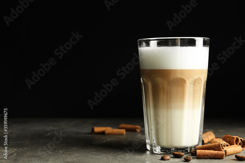 Delicious latte macchiato and cinnamon on grey table against black background, space for text photo