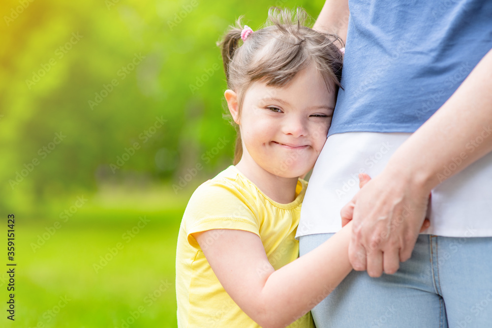 Happy little girl with syndrom down hugs mother in a sunny summer park. Empty space for text Happy little girl with syndrom down hugs mother in a sunny summer park. Empty space for text
