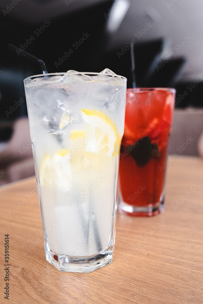 two summer refreshments with ice, lemon, strawberries, mint in tall glasses with a straw on a table in a restaurant. healthy lemonade. out of the house. two summer refreshments with ice, lemon, strawberries, mint in tall glasses with a straw on a table in a restaurant. healthy lemonade. out of the house.