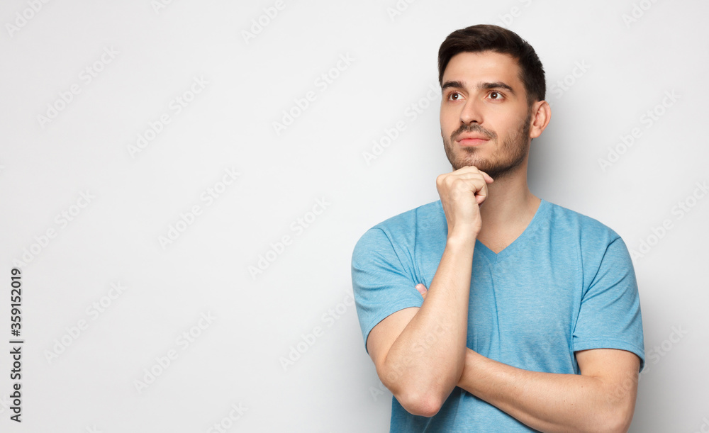 Banner of young man in blue t-shirt with dreamy cheerful expression, thinking, isolated on gray background with copy space for your ads Banner of young man in blue t-shirt with dreamy cheerful expression, thinking, isolated on gray background with copy space for your ads