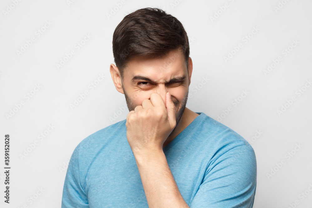 Young man holding his nose as if smelling something rotten and stinky, trying to find source of odor Young man holding his nose as if smelling something rotten and stinky, trying to find source of odor