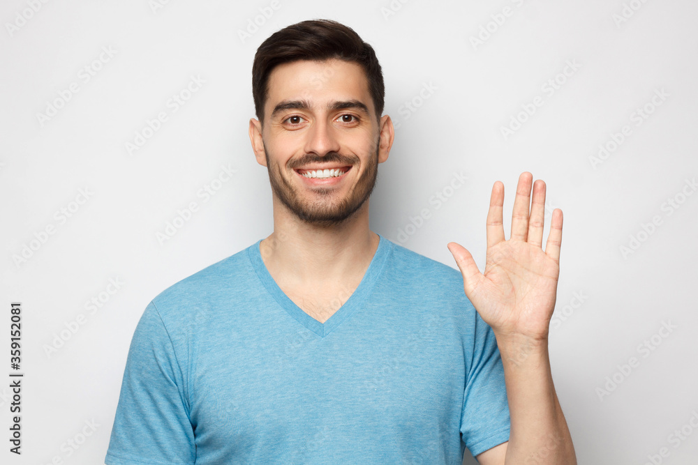Young smiling man greeting someone with open hand, wearing blue tshirt, isolated on gray background Young smiling man greeting someone with open hand, wearing blue tshirt, isolated on gray background
