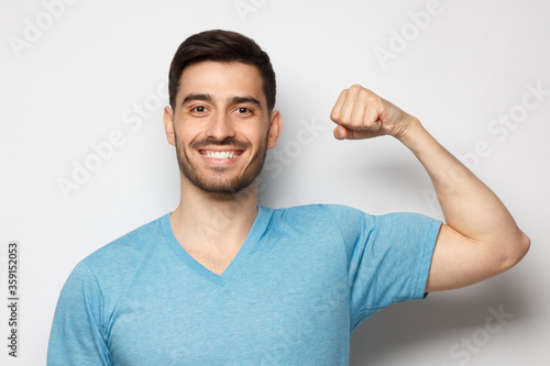 Photos Young strong sporty athletic man in casual blue t-shirt, showing biceps after tr