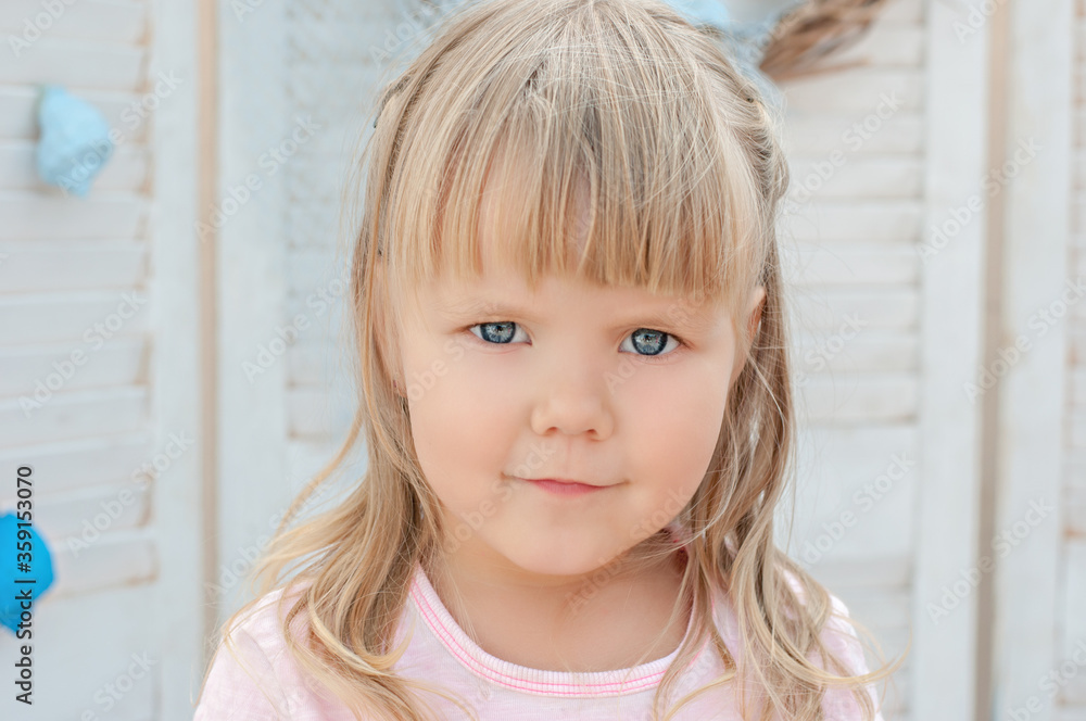 A close-up portrait of a little blonde girl with blue eyes looking at the camera and laughing. Baby plays with shells on the background of marine decoration. Sea adventures and games for children. 