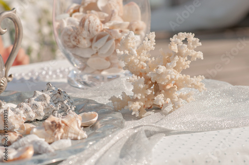 Decoration of holidays, events and weddings in a marine style. On the table are beautiful corals, a variety of shells, pearls, starfish. Unusual interior design of houses apartments. Romantic dinner