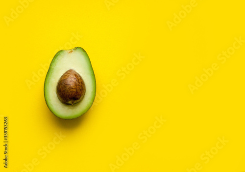 avocado cut in half with the core on a uniform yellow background