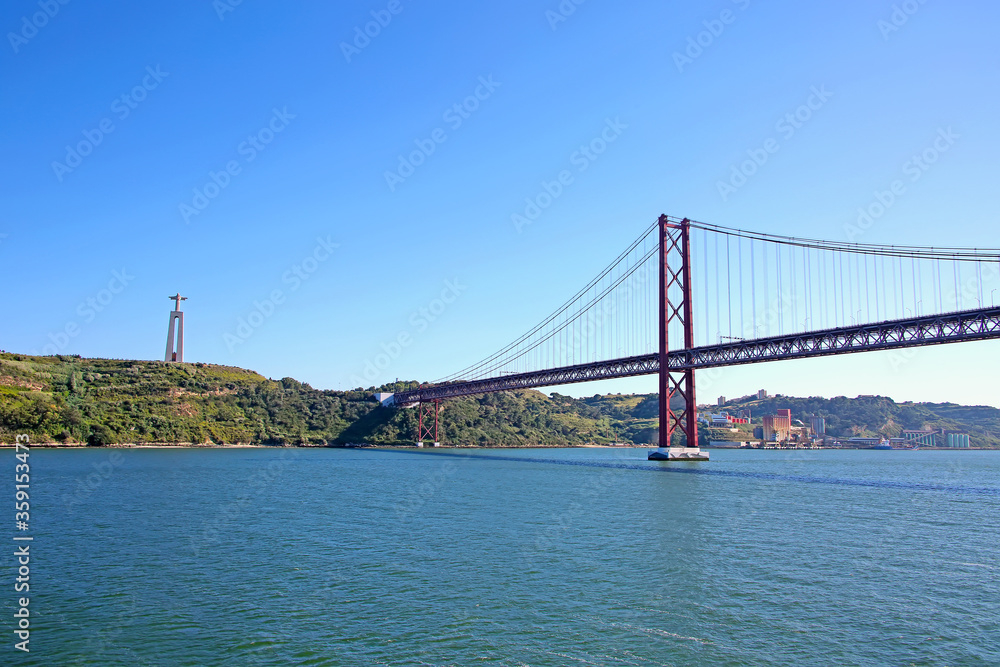 25 de Abril suspension Bridge connecting the city of Lisbon, to the municipality of Almada & the statue of Christ in the background over the Tejo Estuary, Lisbon, Portugal. 25 de Abril suspension Bridge connecting the city of Lisbon, to the municipality of Almada & the statue of Christ in the background over the Tejo Estuary, Lisbon, Portugal.