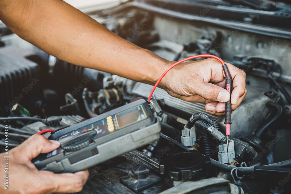 Auto mechanic using measuring equipment tool for fix checking car battery. Concepts of Old car repair service and insurance. Auto mechanic using measuring equipment tool for fix checking car battery. Concepts of Old car repair service and insurance.