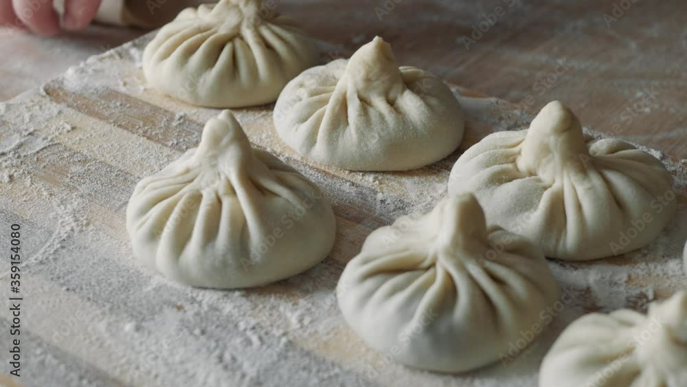 Close up of female chef pinching top of dumpling wrapper and forming khinkali at the kitchen. Close up of female chef pinching top of dumpling wrapper and forming khinkali at the kitchen.