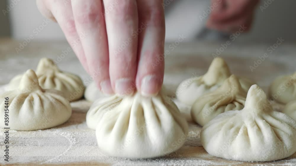 Close up of female chef pinching top of dumpling wrapper and forming khinkali. Shallow depth of focus. Close up of female chef pinching top of dumpling wrapper and forming khinkali. Shallow depth of focus.