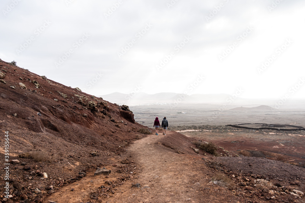 Young couple walking down the hill on the red vulcanic landscape with panoramic view