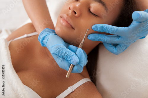 Attractive African woman getting pimples and blackheads removed by professional cosmetician photo