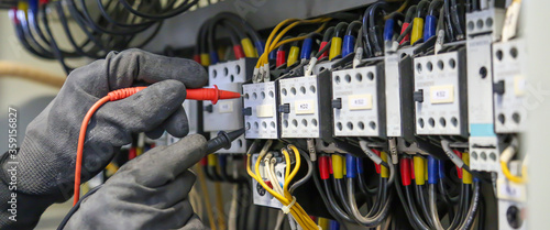 Electrical engineer using digital multi-meter measuring equipment to checking electric current voltage at circuit breaker in main power distribution board. photo