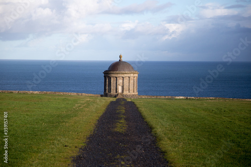 Museenden Temple Ireland auf der wiese mit meer im Hintetgrund und blauem himmel im Sonnenlicht