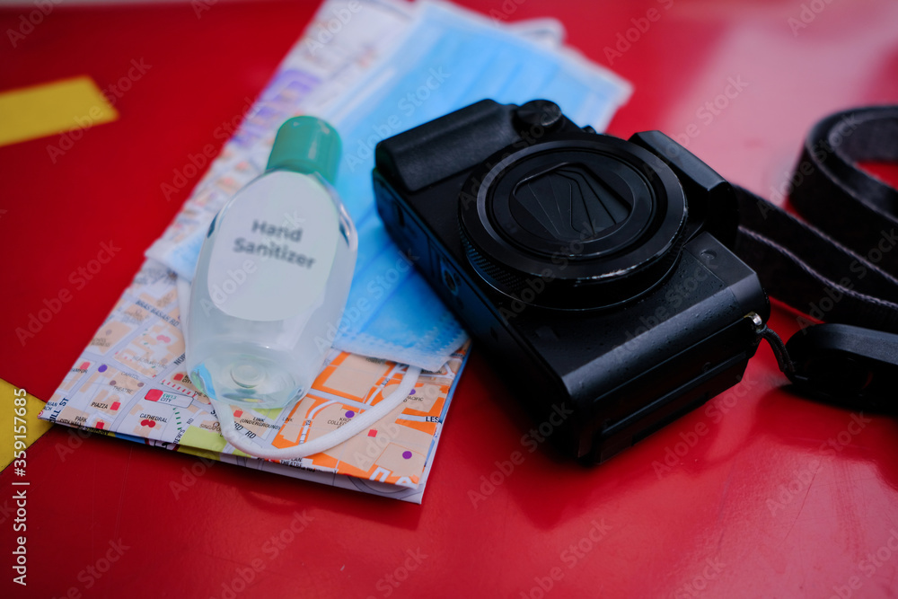 Camera, face mask, hand sanitiser, & map on a bench; Travel essentials concept; essential items to bring when travelling during covid-19; coronavirus outbreak. Selective focus.
