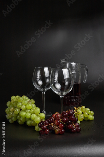 Still life on a black background. A glass wine glass and grape vine.