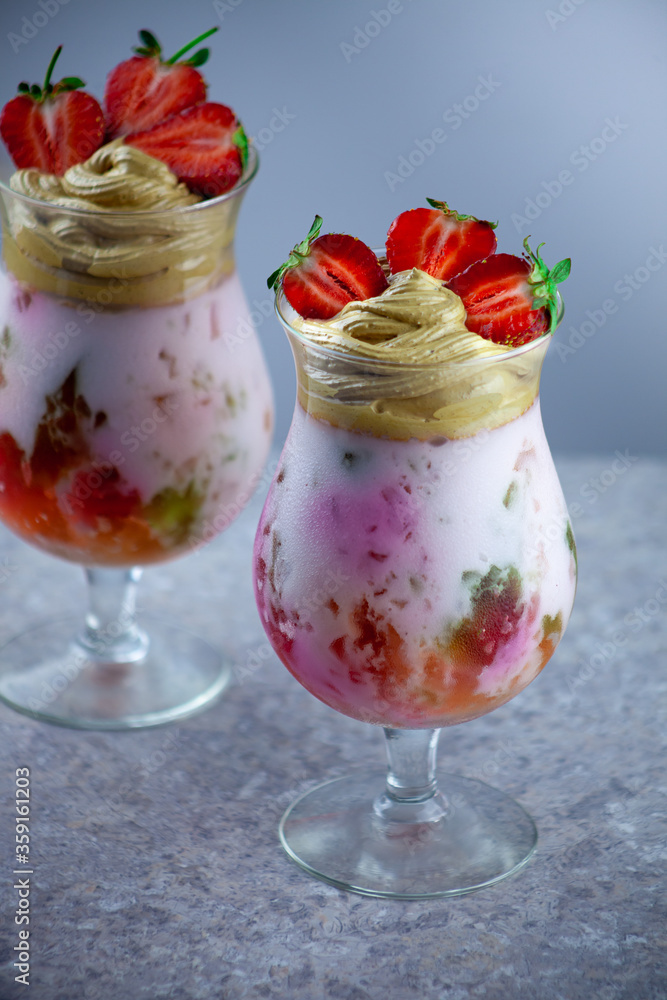 Cold summer dessert. Bowls of layered jelly served on table against light background. Colourful, festive cocktail with sweets jelly in glass. Strawberries, yogurt and chocolate cream close-up. Cold summer dessert. Bowls of layered jelly served on table against light background. Colourful, festive cocktail with sweets jelly in glass. Strawberries, yogurt and chocolate cream close-up.