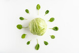 Fresh young green cabbage in the center and leaves of spinach around it on a white table. Vegeterian food. Top view