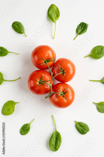 Sprig of fresh red juicy tomatoes in the center and leaves of spinach around it on a white table. Vegeterian food. Vertical. Close-up. Top view