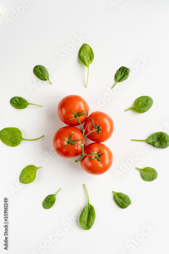 Sprig of fresh red juicy tomatoes in the center and leaves of spinach around it on a white table. Vegeterian food. Vertical. Top view